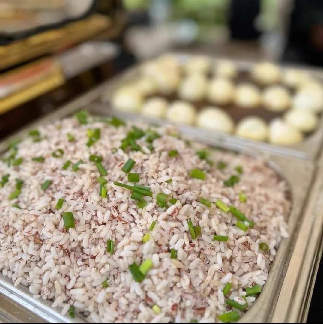 A buffet tray of native rice topped with spring onion beside a tray of moulded moi moi