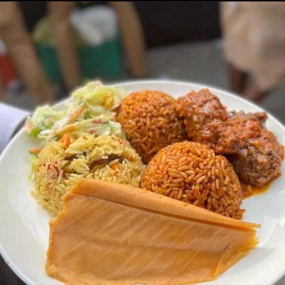 A guest plate of jollof rice, fried rice, amala, stew and salad at an event