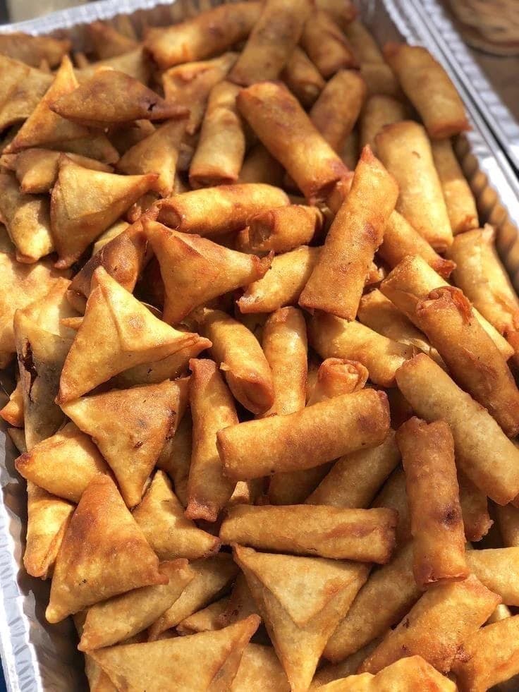 A close view of freshly fried samosas and spring rolls in a foil tray